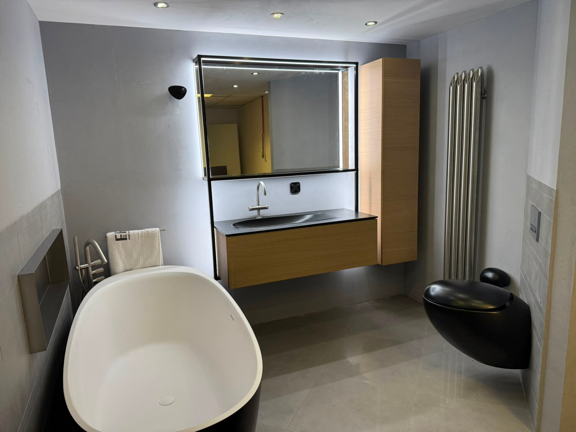 Grote badkameropstelling met hoge kast, radiator en wandcloset